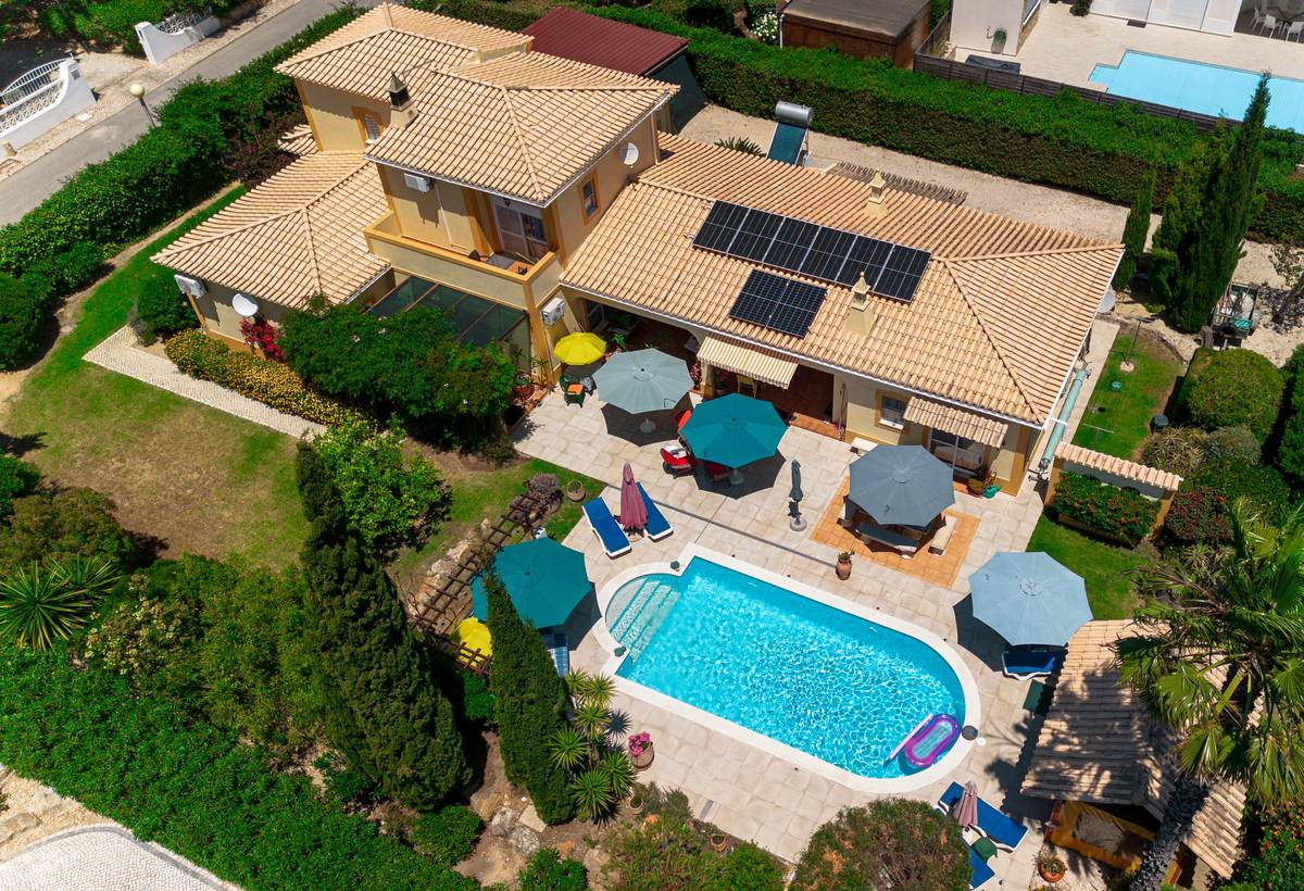 Vue aérienne oblique : la maison, la terrasse et ses parasols, la piscine, l'apatam et le jardin