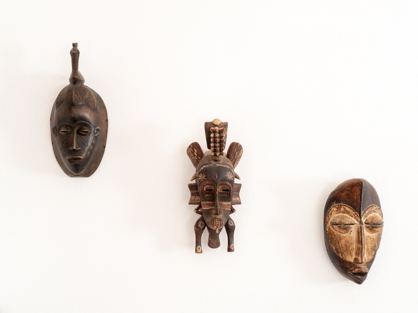 Trois masques africains en bois accrochés à un mur blanc