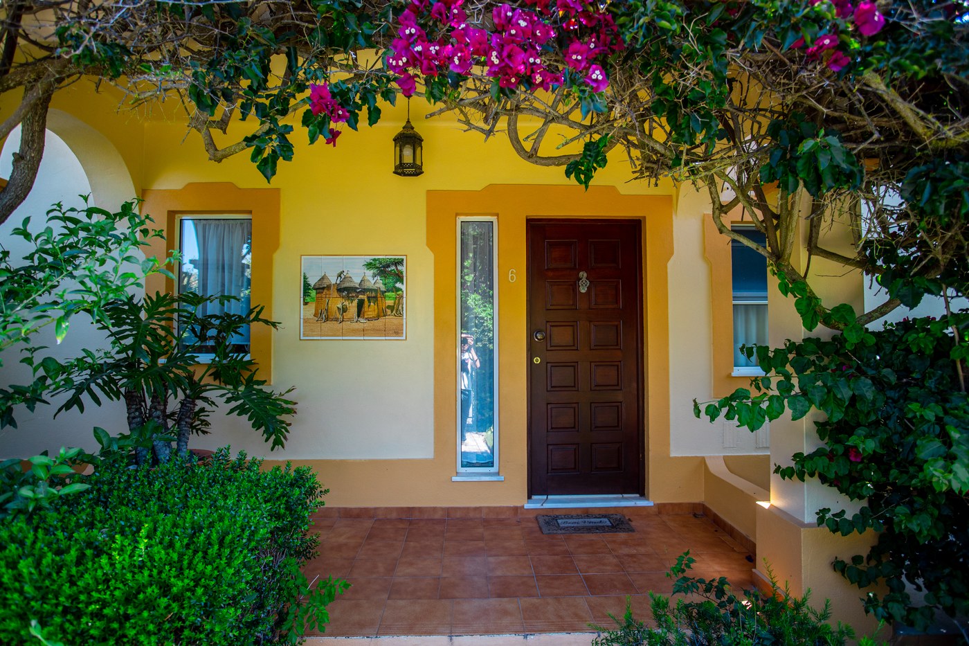 La porte d'entrée de la maison sous les bougainvillées, à côté d'un panneau d'azulejos représentant un village de Tata Somba